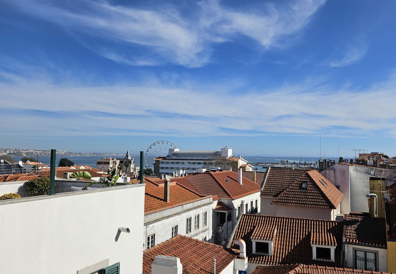 Panorama urbano com telhados vermelhos e céu azul, com o mar à distância. 